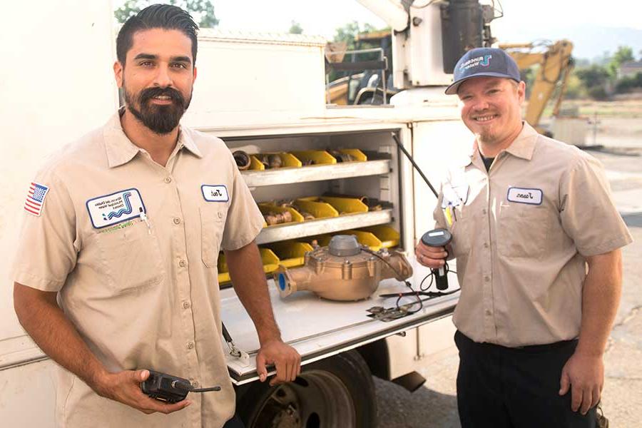 两个面带微笑的水技师站在一辆卡车前.